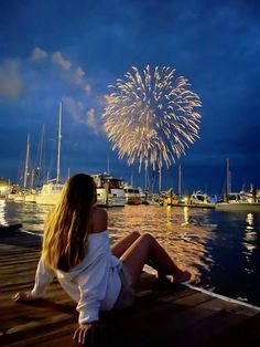 a woman sitting on a dock watching fireworks