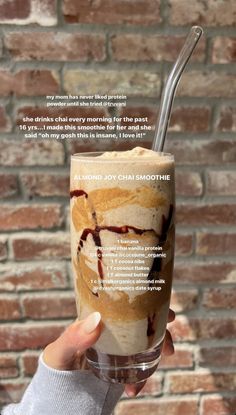 a person holding up a drink in front of a brick wall with words written on it