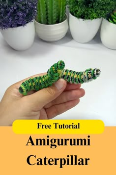 a hand holding a small green and yellow caterpillar on top of a white table