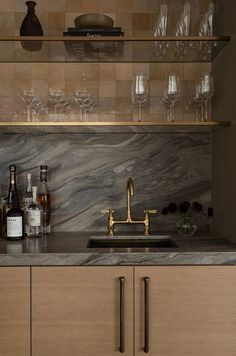 a kitchen with marble counter tops and gold faucet, wine glasses on the shelf