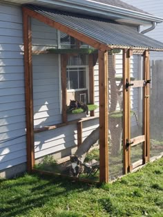 a small chicken coop in the grass next to a house with a cat on it