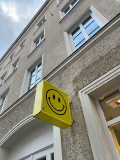 a yellow smiley face sign on the side of a gray building with windows and sky in the background