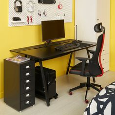 a desk with a computer on it in front of a yellow wall and black filing cabinets