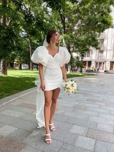 a woman in a short white dress walking down the street with her bouquet on her hand