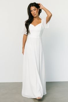 a woman in a white dress posing for the camera with her hand on her head