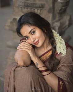 a woman sitting on the ground with her arms crossed and wearing a flower in her hair