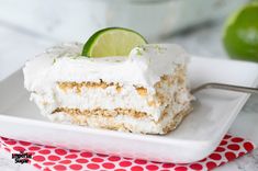 a piece of cake on a white plate with a lime slice and a red polka dot napkin