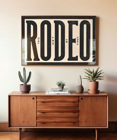 a wooden sideboard with two plants on top and a framed poster above it that says rodeo