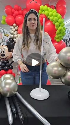 a woman standing in front of balloons and mickey mouse figurines on a table