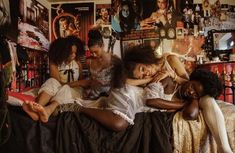 three women are sitting on a bed in a room with posters all over the wall