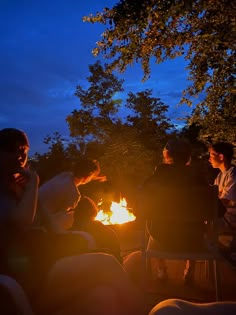 people sitting around a campfire at night with one person holding something in his hand