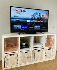 a flat screen tv sitting on top of a white entertainment center next to wicker baskets