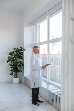 a man in a white lab coat standing by a window