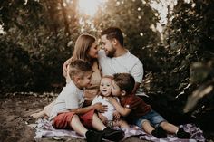 a family is sitting on a blanket in the woods with their two children and one adult