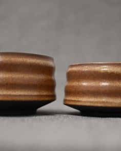 two wooden bowls sitting next to each other on top of a gray surface with no one in it