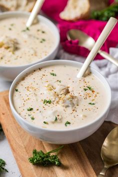 two white bowls filled with soup and garnished with parsley on a cutting board