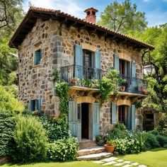 an old stone house with blue shutters and flowers on the front door is surrounded by greenery