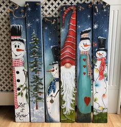 four snowmen painted on wooden boards with christmas decorations