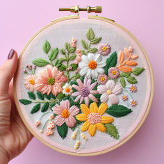 a hand is holding up a embroidery hoop with flowers in it on a pink background