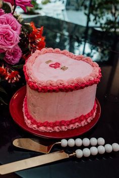 a pink cake sitting on top of a red plate next to flowers and a knife