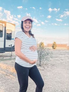 a pregnant woman standing in front of an rv with her hands on her stomach and smiling