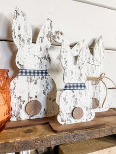 two white wooden rabbits sitting on top of a shelf next to an orange glass vase