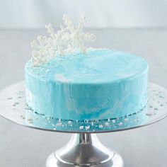 a blue frosted cake with white snowflakes on top sits on a silver plate