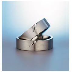 two silver wedding rings with one diamond on top and the other in the middle, against a blue background