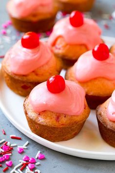 cupcakes with pink frosting and cherries on a plate