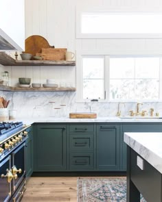 a kitchen with green cabinets and marble counter tops, an island in front of the stove