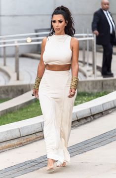 a woman walking down the street wearing a white outfit and matching heels with her hand on her hip