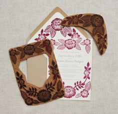 the wedding card is decorated with red and brown flowers on white paper, along with a wooden frame