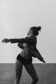 a black and white photo of a woman playing with a frisbee in an empty room