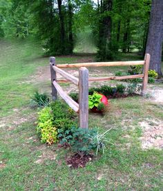 a wooden fence in the middle of a grassy area with flowers and plants around it