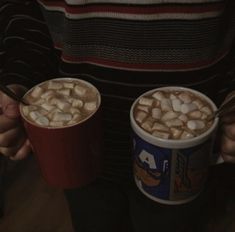 two cups of hot chocolate and marshmallows are held by someone's hands