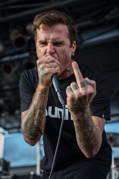 a man with tattoos on his arms holding a microphone in front of him and making the peace sign