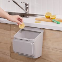 a person holding a coin in front of a kitchen sink with a trash can and cutting board on the counter