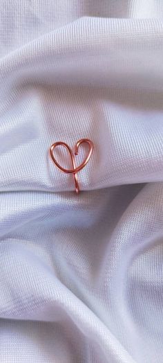 a heart shaped ring sitting on top of a white cloth covered in pink threads