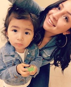 a woman holding a small child in her lap and smiling at the camera while they both have their hands on each other's shoulders