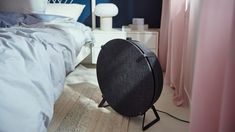 a black round object sitting on top of a white floor next to a pink bed