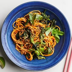 a blue bowl filled with noodles and vegetables next to chopsticks on a white table