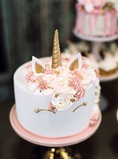 there is a white cake with pink flowers and a gold horn on top that says unicorn