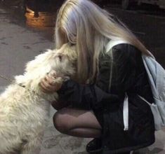 a woman is petting a white dog on the street