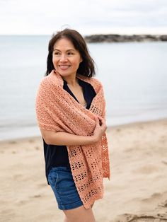 a woman standing on top of a sandy beach next to the ocean wearing a shawl