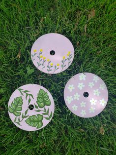 three frisbees sitting in the grass with flowers painted on them