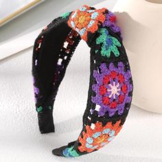 a crocheted headband with colorful flowers on it sitting next to a white vase