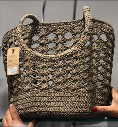 a crocheted purse is being held up by a woman's hand with a tag on it