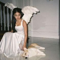 a woman in white dress sitting next to a dog with wings on its head and tail