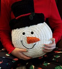 a woman is holding a crocheted snowman pillow