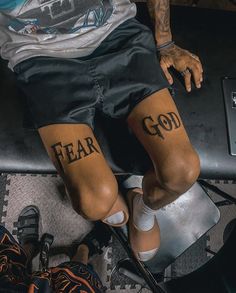 a man sitting on top of a metal bench with his feet covered in tattoos that say fear and god